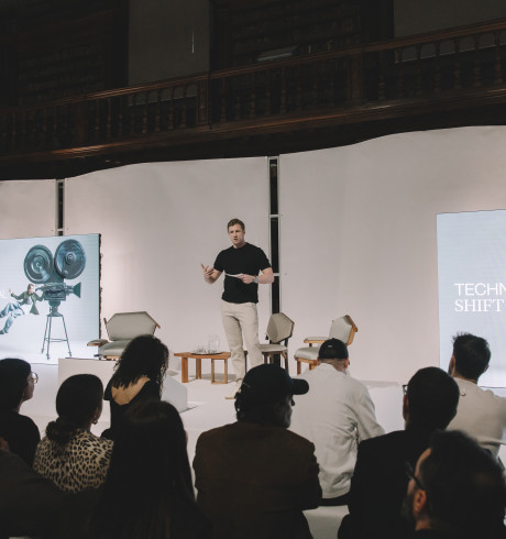 David Schneider spricht auf der Bühne; auf den Bildschirmen hinter ihm steht: Technological Shift