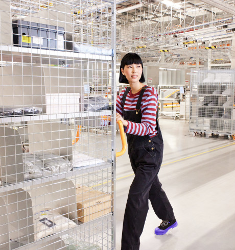 Young woman in dungarees, work boots and a striped shirt pushing a trolley in a warehouse