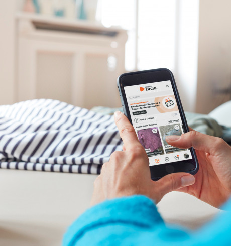 Hands holding a smartphone in a home environment, Zircle app showing on the screen