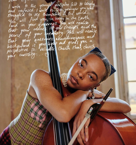 a Black woman hugging a double base in a patterned top, with a hand-written text covering part of the photo