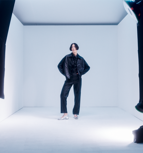 Female fashion model on set; white background, camera equipment in the foreground framing her