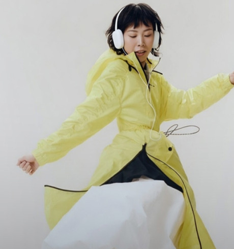 A female model dancing with over-ear headphones and wearing a bright yellow raincoat