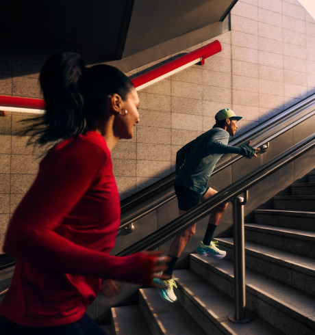 Two runners speeding up the stairs from what looks like a subway station, from the dark out towards the light