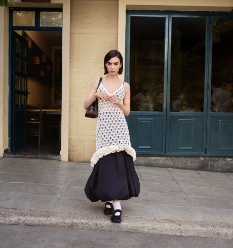 Lily Collins posing in front of what looks like a quaint little café