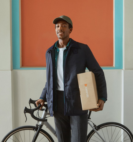 A man pushing a bike holds a Zalando package.