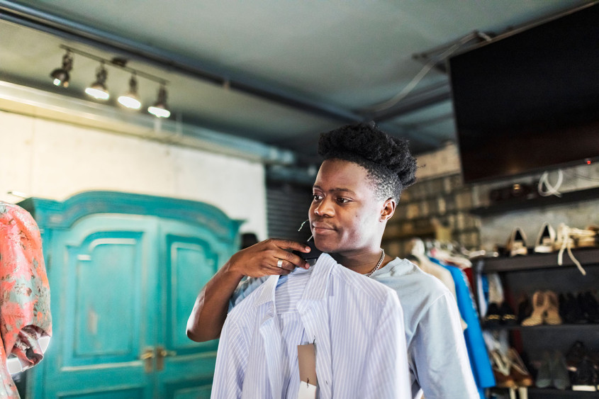 (Photo: iStock.com/JulPo) Man holding new clothes in front of the mirror in a shop setting