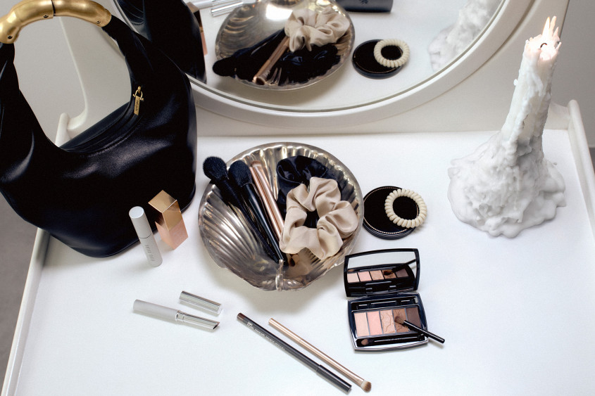 A dressing table with beauty products, a black handbag and a lit candle