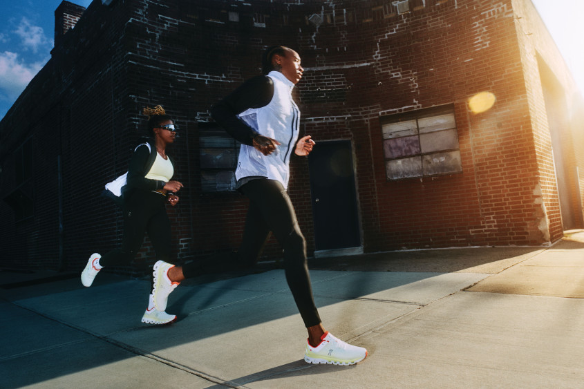 Two runners in sports wear rounding a street corner into the sunlight