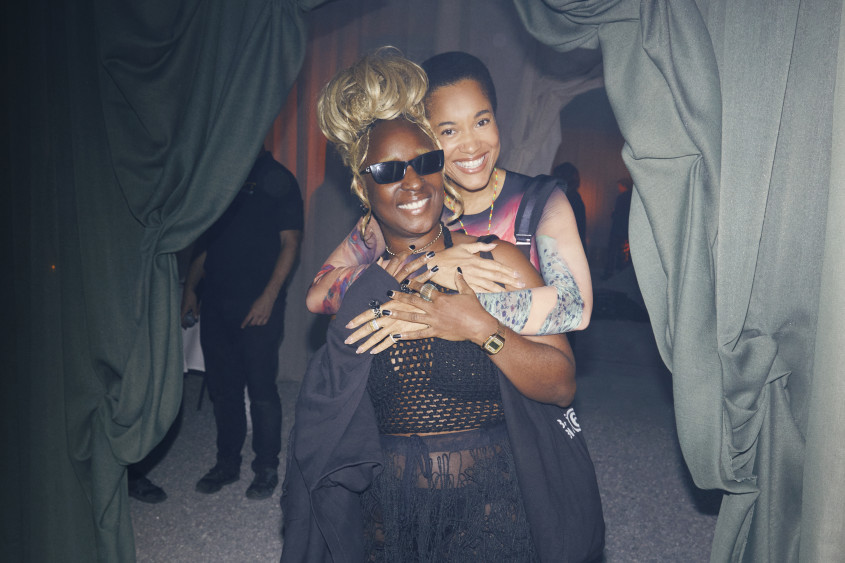 Bubu Ogisi posing from the camera, another woman is hugging her from behind looking over her shoulder