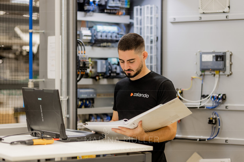 Logistics employee in a warehouse setting holding a folder and looking at a computer