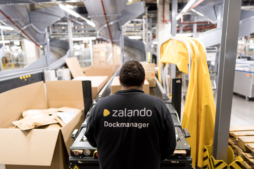 Warehouse setting: lots of parcels on a conveyor belt, dockmanager seen from behind