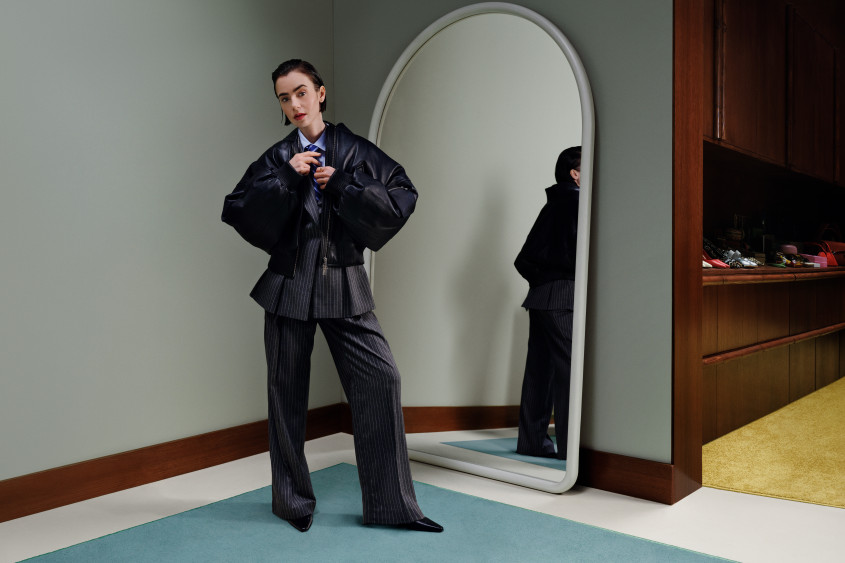 Lily Collins in an oversized statement business suit posing for the camera in front of a big mirror