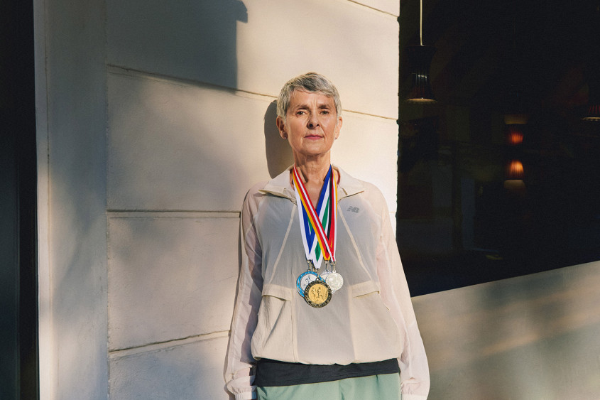 Woman with short grey hair in running gear posing for the camera with three medals around her neck
