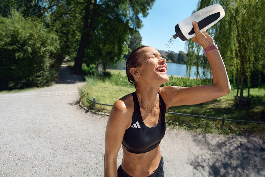 Sunny day, young female runner pouring water over her face, laughing