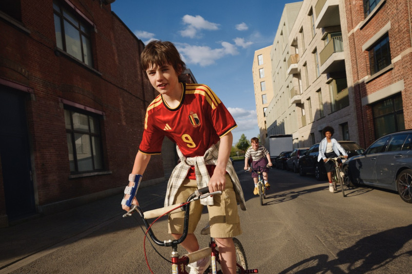 Three boys riding their bikes in the street, one of them wearing an RBFA jersey