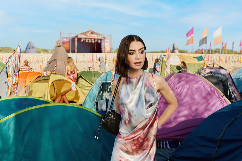 Lily Collins wearing a colourful dress amidst small tents in a summery festival area