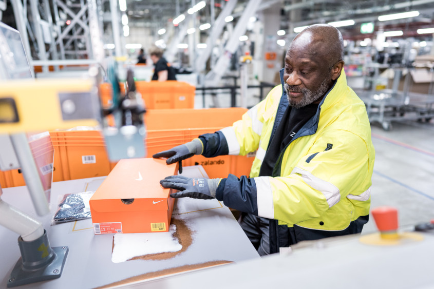 A logistics employee handling an orange shoe box