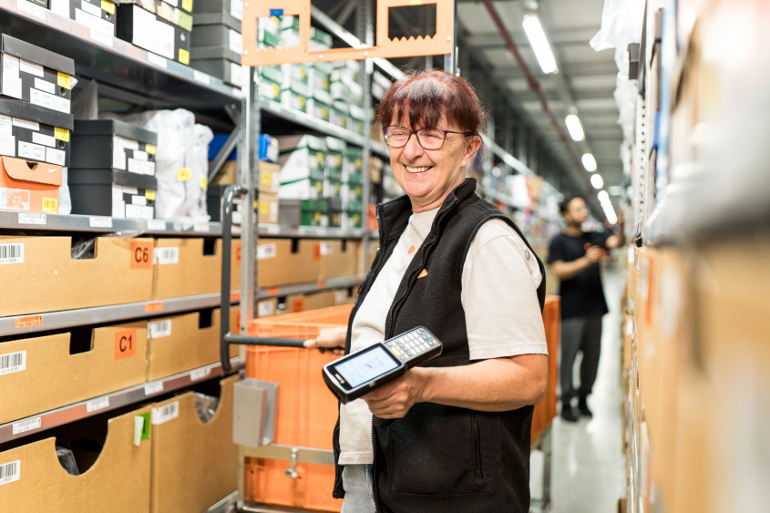 Smiling logistics employee between high shelves in a warehouse setting