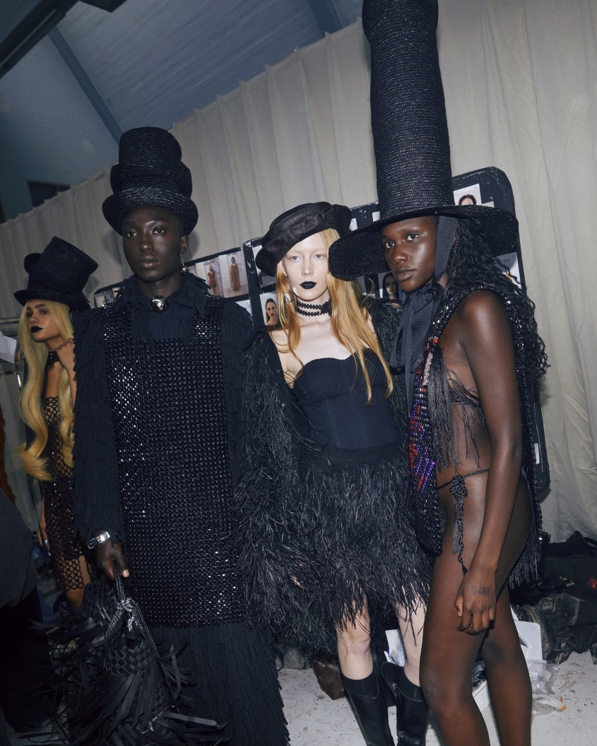 Three fashion models in various black outfits posing together backstage