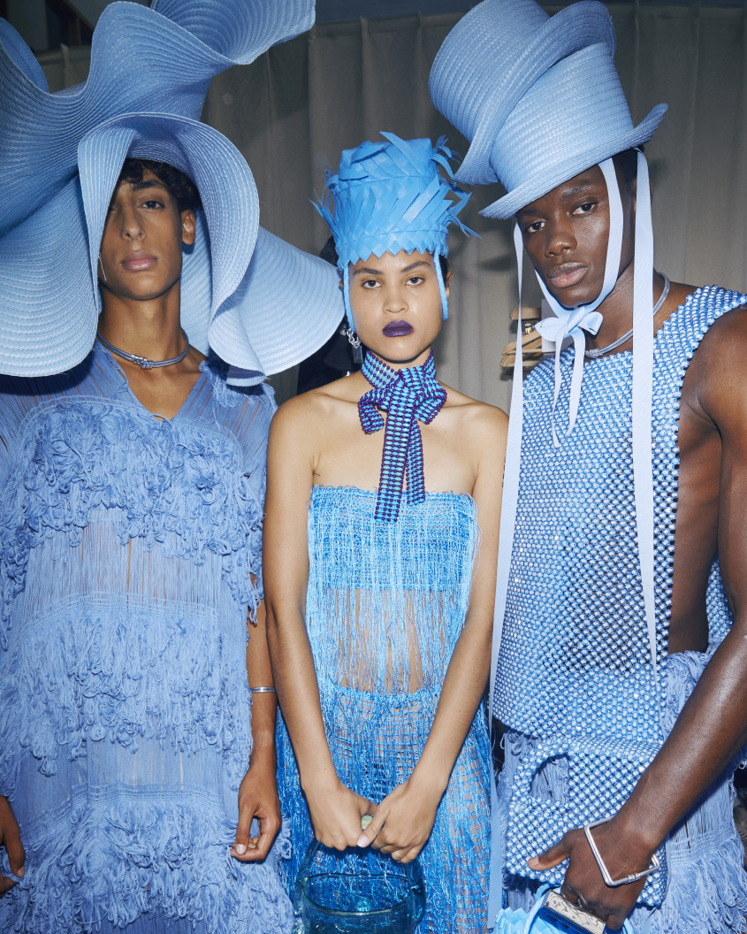 Three fashion models in various blue outfits posing together backstage