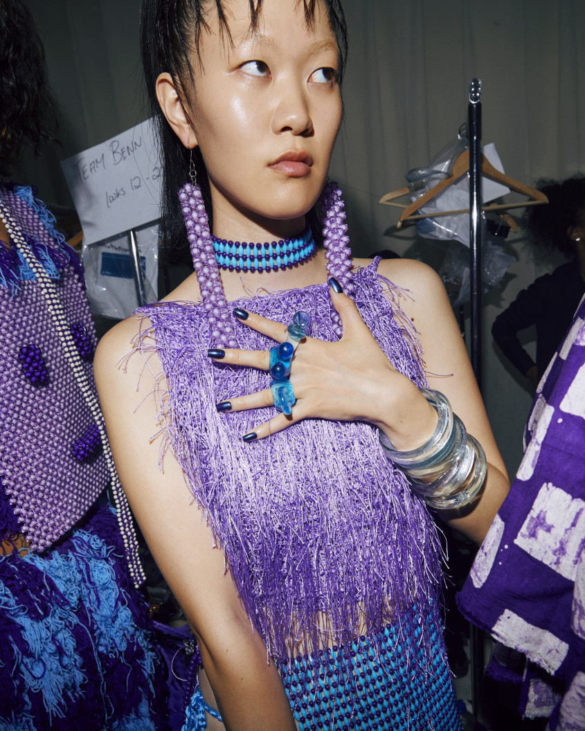 Fashion model backstage clutching her chest to show off three oversized blue-ish rings on her fingers