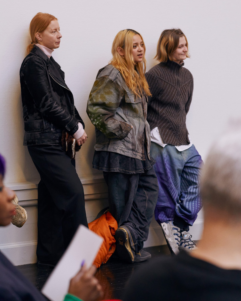 Three people standing up, listening to what is being said on stage