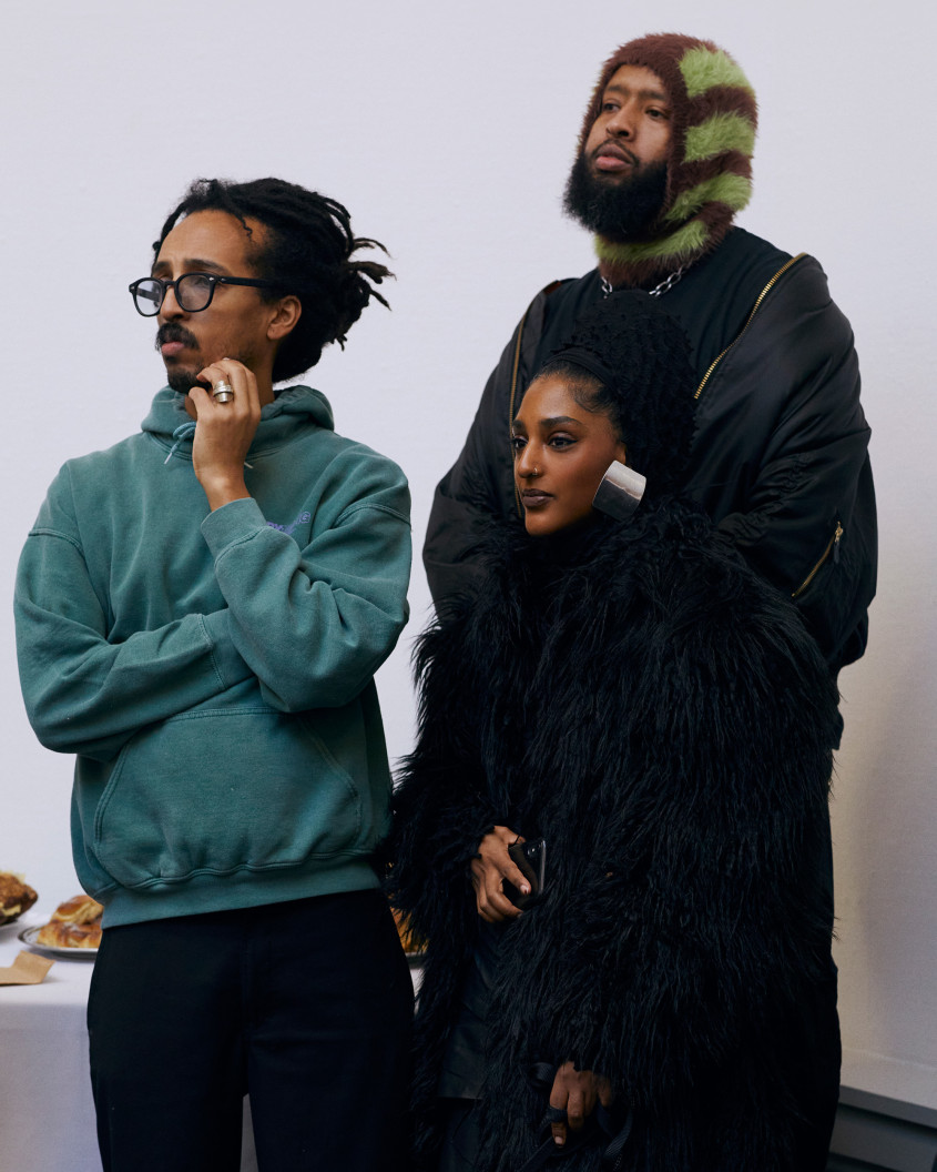 Three people standing up, listening to what is being said on stage