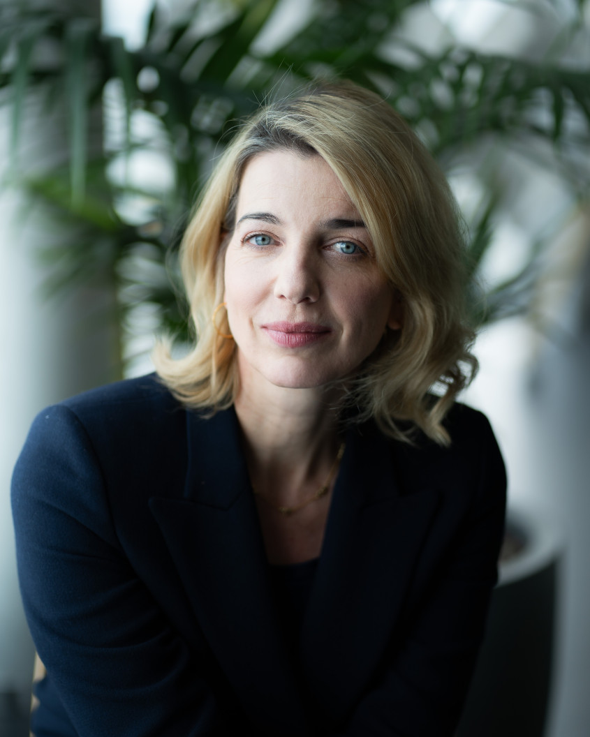 Portrait of Joanna Rogers, soft light from a window and a big plant in the background