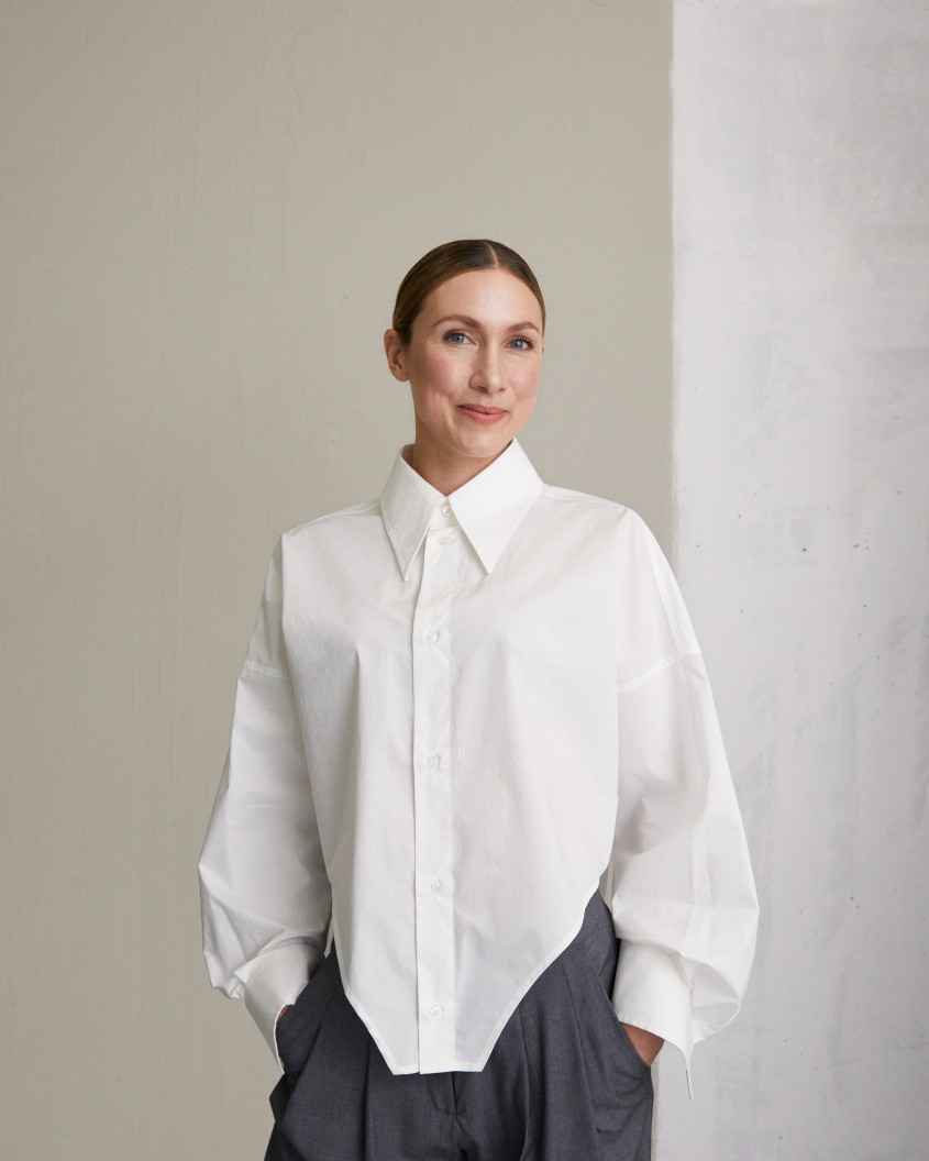 Lena-Sophie Roeper in an oversized white shirt and grey dress trousers posing in front of a white wall