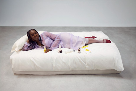 Sophie Carbonari lounging on a big white bed, displaying a variety of beauty products