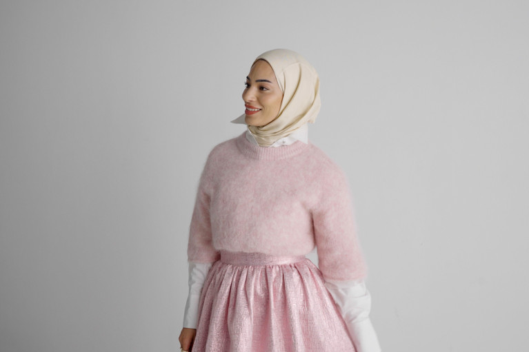 Model looking to the side, wearing a pink long skirt, a pink woolen oversized sweater and matching hijab.