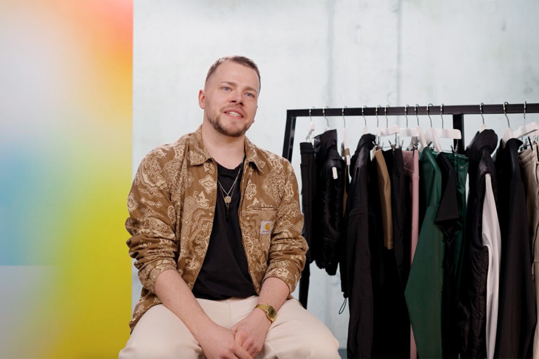 Private Label Senior Fashion Designer Philipp Hammermeister during his interview, sitting on a stool next to a clothes rack