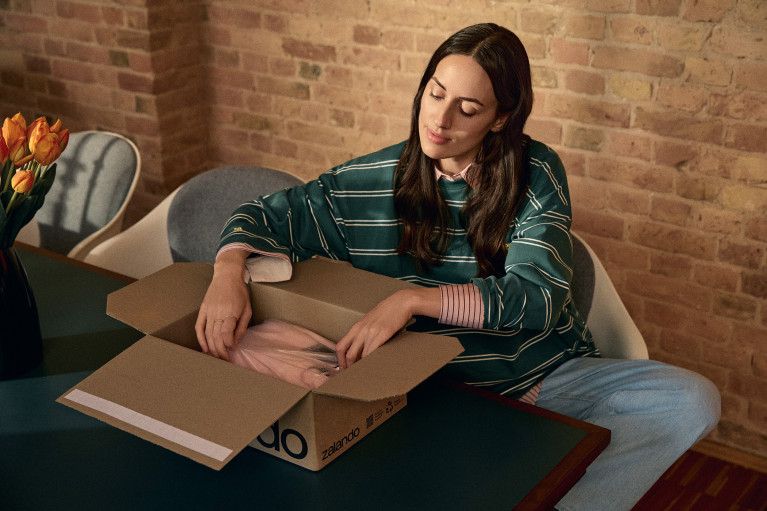 A woman sitting comfortably at a table unpacking a Zalando parcel
