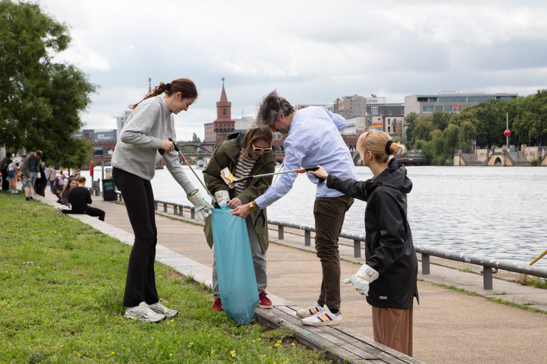 A group of volunteers collecting garbage at Berlin's East side gallery park; Oberbaumbrücke and Spree in the background