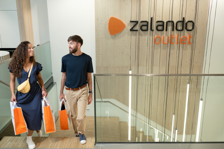 two customers with orange Zalando shopping bags coming up the stairs inside an outlet store