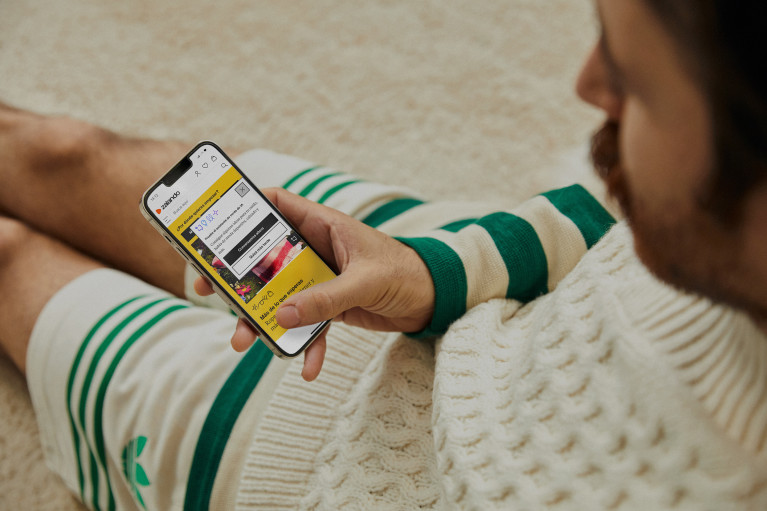 A Zalando customer sitting on the floor looking at the Zalando fashion assistant on his mobile phone; only hand and part of their legs are visible