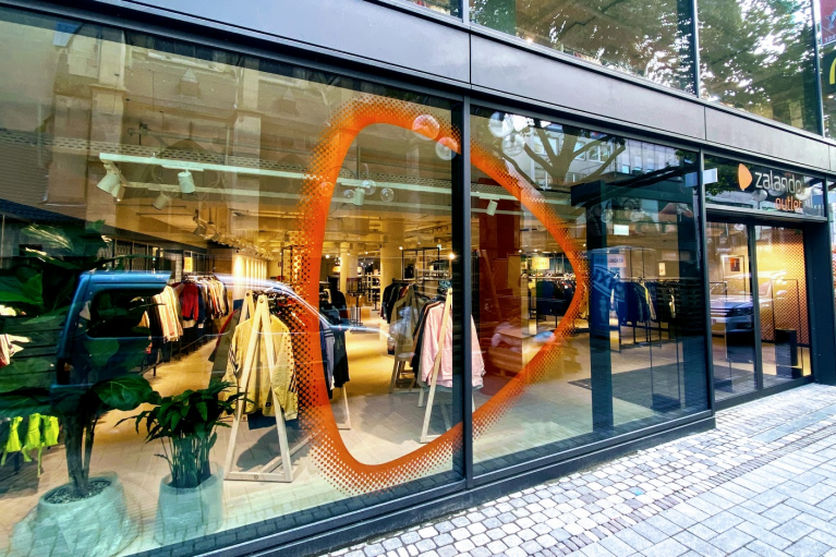 Storefront, Zalando brand beacon on a glass front, clothes can be seen inside