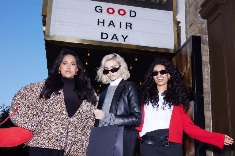 Three models posing for the camera underneath a sign reading: Good Hair Day