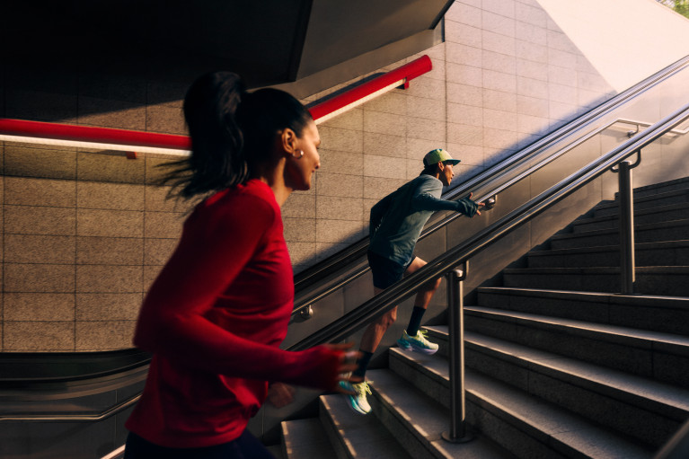 Two runners speeding up the stairs from what looks like a subway station, from the dark out towards the light
