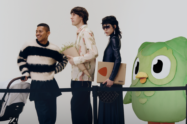 Three people with a baby stroller are waiting behind a barrier with the duolingo owl