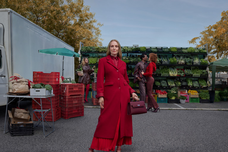 Uma Thurman stands in a red coat at a marketplace for our Autumn Winter campaign 2025